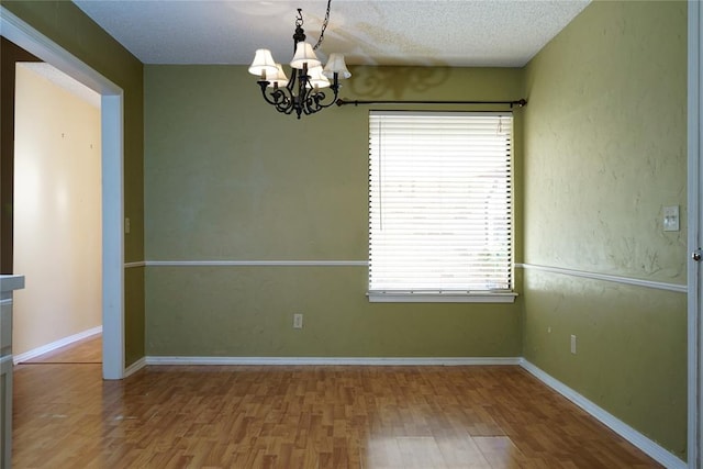 empty room featuring hardwood / wood-style floors, a textured ceiling, and an inviting chandelier