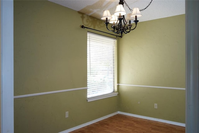 unfurnished room with hardwood / wood-style flooring, a textured ceiling, a wealth of natural light, and a chandelier