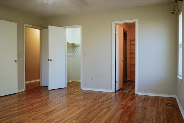 unfurnished bedroom featuring wood-type flooring, a walk in closet, a textured ceiling, and a closet