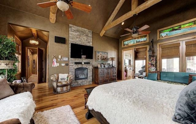 bedroom with ceiling fan, a stone fireplace, beamed ceiling, high vaulted ceiling, and light hardwood / wood-style floors