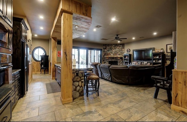 kitchen with a kitchen breakfast bar, oven, ceiling fan, light stone countertops, and a fireplace