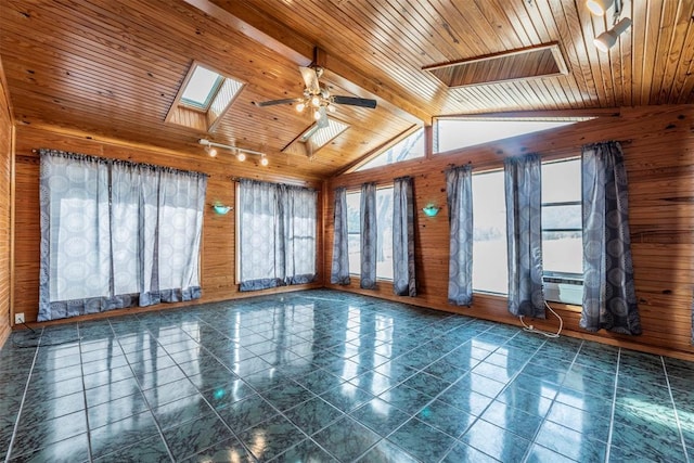 tiled empty room featuring ceiling fan, wooden ceiling, vaulted ceiling with skylight, and wood walls