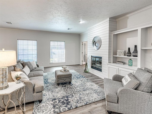 living room featuring hardwood / wood-style floors, a large fireplace, a textured ceiling, and crown molding