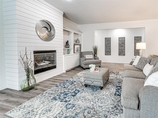 living room with built in shelves, ornamental molding, a textured ceiling, a fireplace, and wood-type flooring