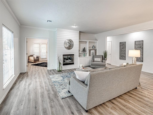 living room featuring a textured ceiling, light wood-type flooring, a large fireplace, and crown molding