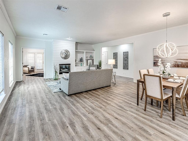 living room featuring light wood-type flooring, a large fireplace, crown molding, and a notable chandelier