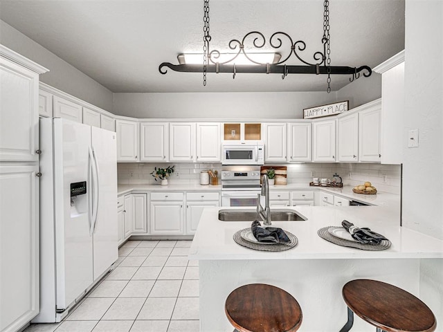 kitchen with white cabinetry, sink, kitchen peninsula, white appliances, and a kitchen bar