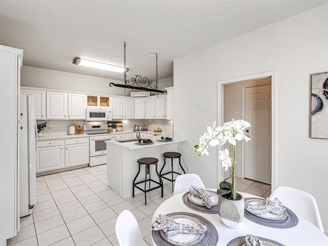 kitchen with a kitchen bar, tasteful backsplash, white appliances, sink, and white cabinetry