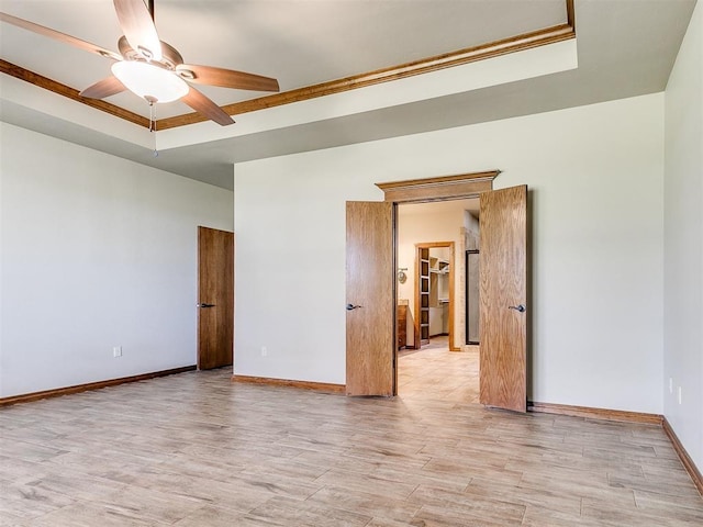 empty room featuring ceiling fan, a raised ceiling, and light wood-type flooring