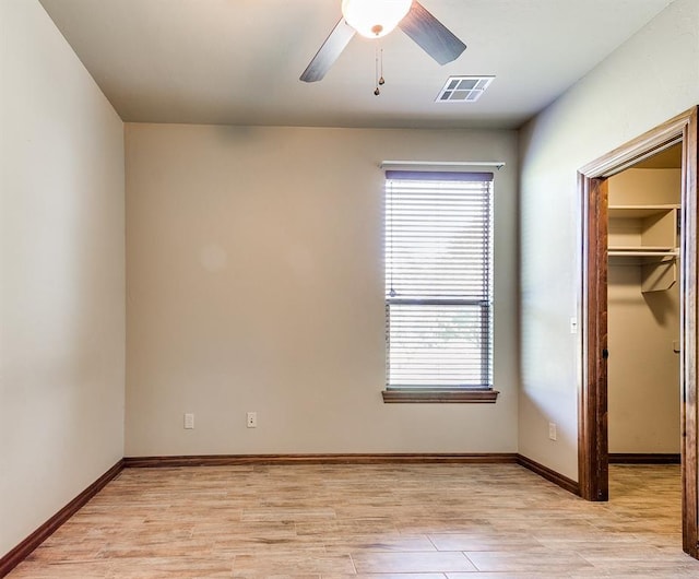 unfurnished bedroom featuring a walk in closet, light hardwood / wood-style floors, a closet, and ceiling fan