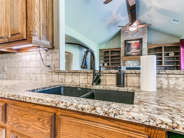 kitchen with sink, vaulted ceiling, ceiling fan, light stone countertops, and backsplash