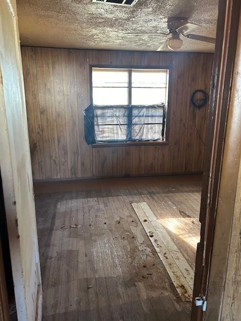 empty room with ceiling fan, wooden walls, and dark hardwood / wood-style floors