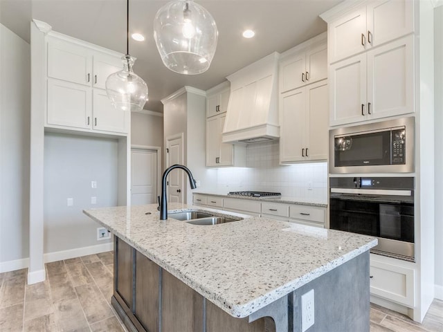 kitchen with custom exhaust hood, stainless steel appliances, a kitchen island with sink, sink, and white cabinets