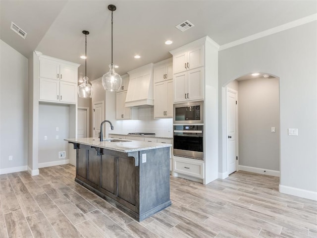 kitchen featuring premium range hood, stainless steel appliances, sink, pendant lighting, and an island with sink