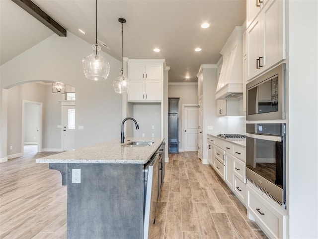 kitchen with sink, hanging light fixtures, stainless steel appliances, light hardwood / wood-style floors, and a kitchen island with sink