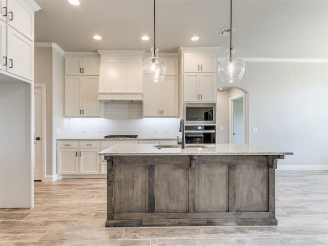 kitchen featuring pendant lighting, a center island with sink, sink, appliances with stainless steel finishes, and light stone counters