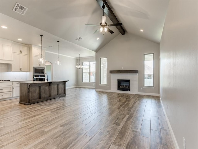 kitchen featuring white cabinets, light wood-type flooring, ceiling fan with notable chandelier, and a kitchen island with sink