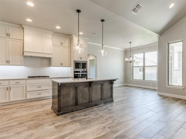 kitchen featuring pendant lighting, stainless steel appliances, a kitchen island with sink, and light hardwood / wood-style flooring