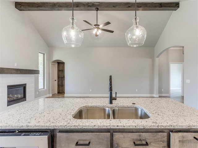 kitchen with vaulted ceiling with beams, light stone counters, sink, and a fireplace