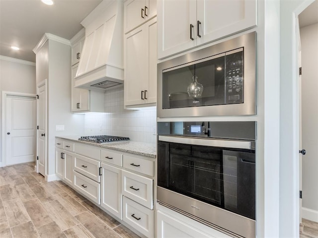 kitchen featuring decorative backsplash, custom range hood, appliances with stainless steel finishes, light hardwood / wood-style floors, and white cabinetry