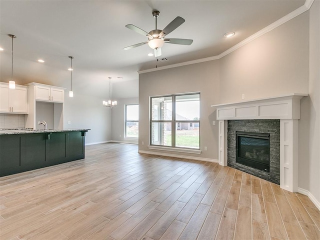 unfurnished living room with ceiling fan with notable chandelier, light wood-type flooring, a fireplace, and crown molding