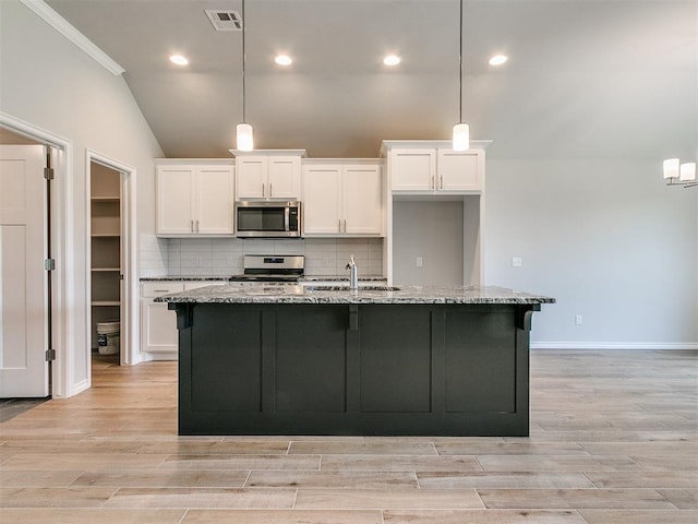 kitchen featuring a kitchen island with sink, light stone counters, pendant lighting, and stainless steel appliances