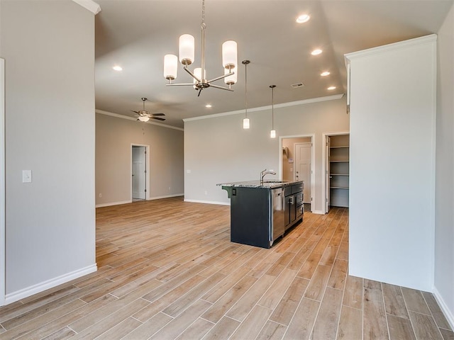 kitchen featuring ceiling fan with notable chandelier, hanging light fixtures, light wood-type flooring, an island with sink, and ornamental molding