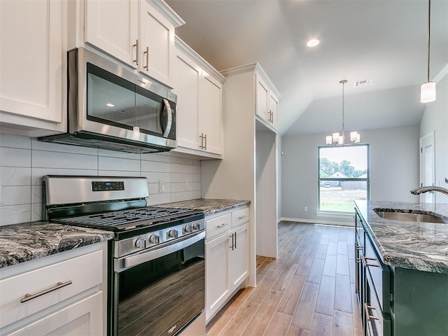 kitchen with sink, stainless steel appliances, dark stone countertops, pendant lighting, and white cabinets