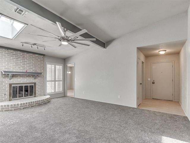 unfurnished living room with beam ceiling, light colored carpet, a brick fireplace, and ceiling fan