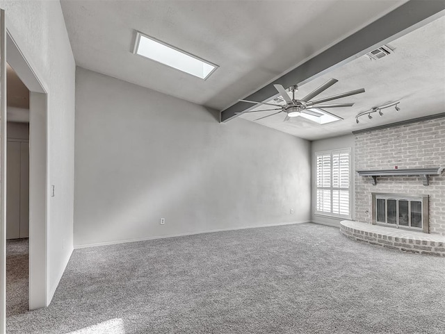 unfurnished living room featuring track lighting, ceiling fan, a fireplace, beamed ceiling, and carpet floors