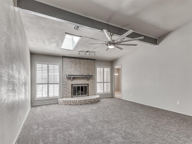 unfurnished living room featuring ceiling fan, beam ceiling, carpet floors, and a brick fireplace