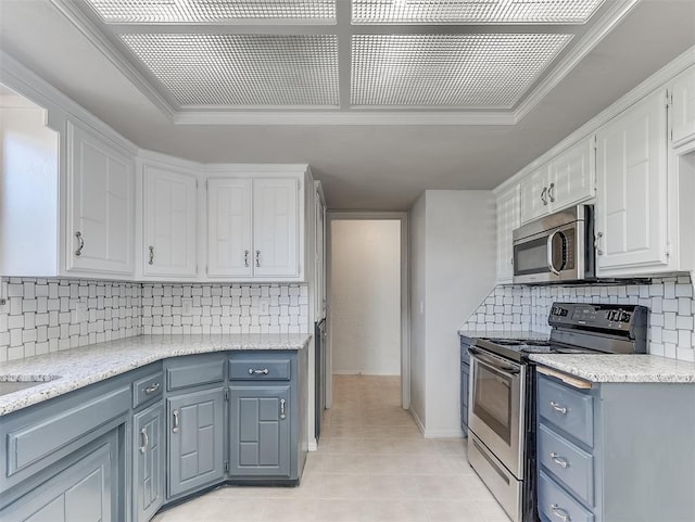 kitchen featuring backsplash, light tile patterned floors, ornamental molding, white cabinetry, and stainless steel appliances