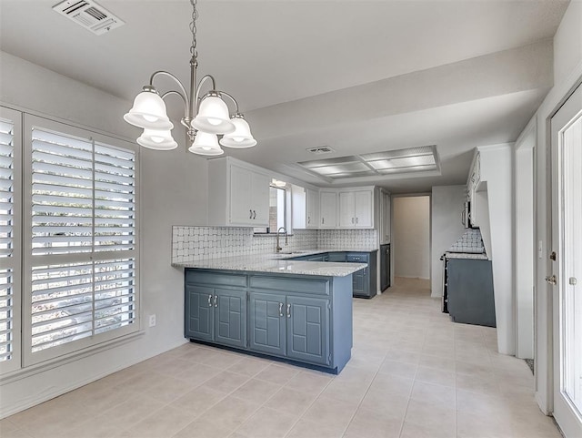 kitchen with kitchen peninsula, tasteful backsplash, an inviting chandelier, white cabinetry, and hanging light fixtures