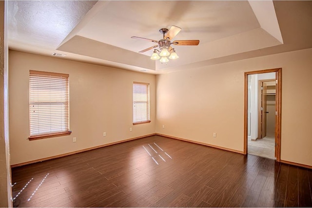 empty room with dark hardwood / wood-style floors, ceiling fan, and a tray ceiling