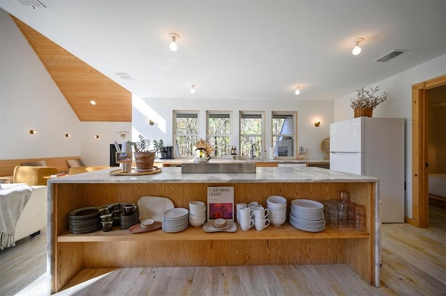 kitchen featuring white refrigerator, light stone counters, light hardwood / wood-style flooring, and sink