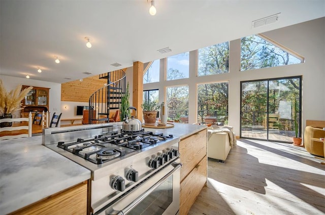 kitchen featuring light hardwood / wood-style floors, high end range, light brown cabinetry, and high vaulted ceiling