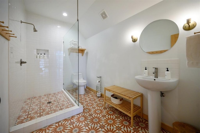 bathroom featuring a tile shower, lofted ceiling, and toilet