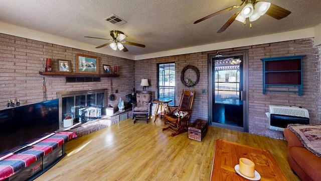 living room with a textured ceiling, heating unit, a brick fireplace, and light hardwood / wood-style floors