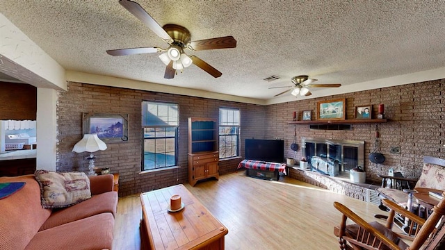 living room featuring brick wall, light hardwood / wood-style floors, a textured ceiling, and a brick fireplace