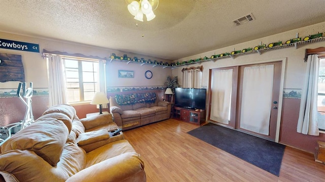 living room featuring a textured ceiling, light wood-type flooring, and ceiling fan