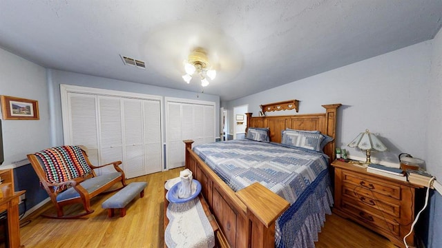 bedroom with ceiling fan, multiple closets, and light hardwood / wood-style flooring