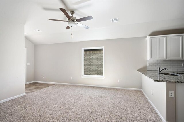 unfurnished living room featuring ceiling fan, light colored carpet, sink, and vaulted ceiling