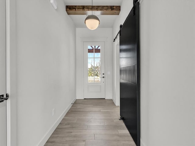 doorway to outside featuring a barn door, light wood-type flooring, and beam ceiling