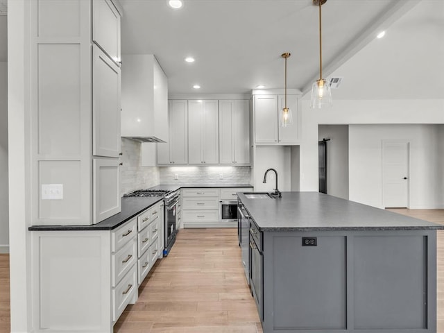 kitchen featuring custom exhaust hood, high end stainless steel range oven, sink, white cabinets, and hanging light fixtures