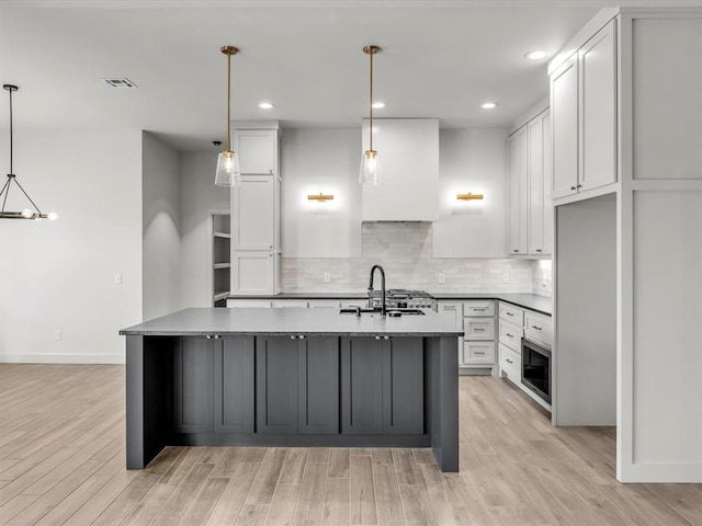 kitchen with sink, white cabinets, pendant lighting, and a center island with sink