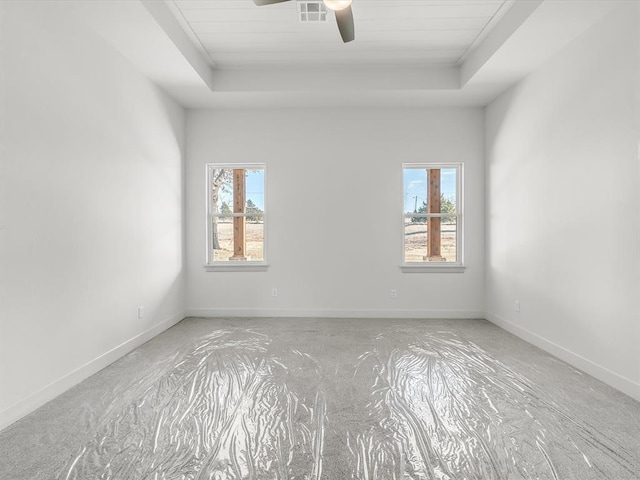 unfurnished room with a raised ceiling, ceiling fan, and a healthy amount of sunlight