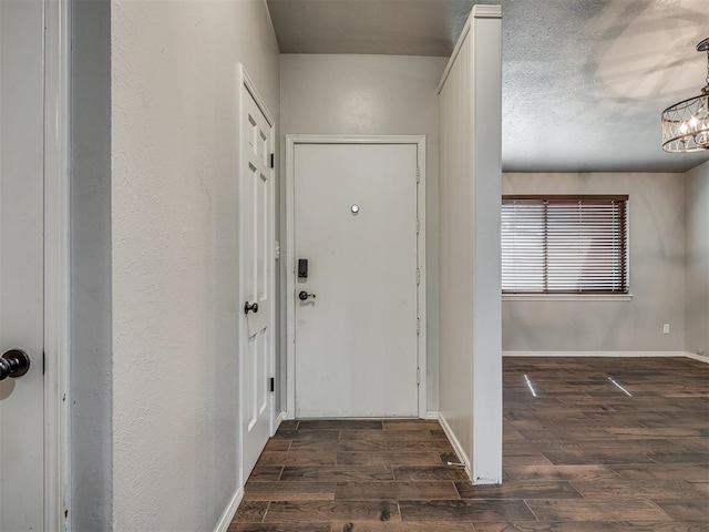 doorway to outside featuring a textured ceiling, dark hardwood / wood-style floors, and an inviting chandelier