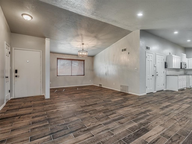 unfurnished living room with a textured ceiling, lofted ceiling, dark wood-type flooring, and a chandelier