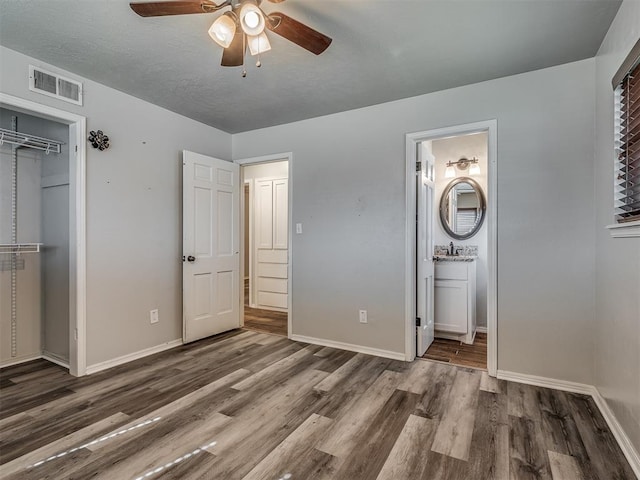 unfurnished bedroom with ensuite bathroom, ceiling fan, dark hardwood / wood-style floors, a textured ceiling, and a closet