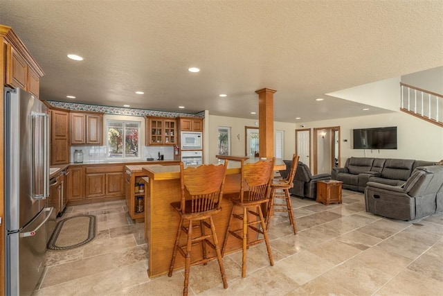 kitchen with white appliances, decorative backsplash, a textured ceiling, a kitchen bar, and decorative columns